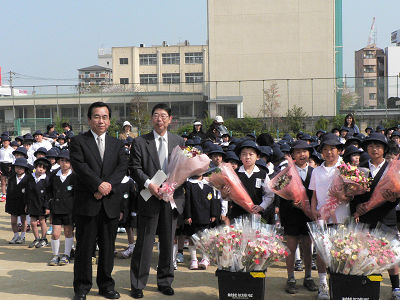 花育企画として地元小学校に花束をプレゼント。（左から）大西なにわ花いちば社長、横堤小学校長