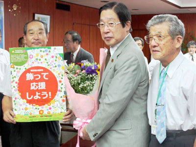 被災地産の花束を手に鹿野農水大臣(中央)。(右)は都倉会長